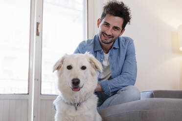 Lächelnde Mitte erwachsenen Mann mit niedlichen Hund im Wohnzimmer zu Hause - EIF01130