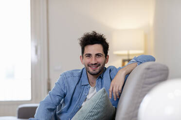 Lächelnder Mann im mittleren Erwachsenenalter, der zu Hause auf dem Sofa sitzt - EIF01137