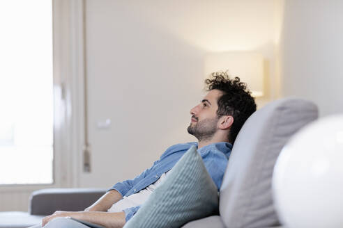 Mid adult man day dreaming while sitting on sofa in living room - EIF01138