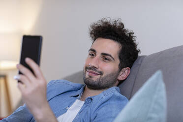 Lächelnder Mann mit Smartphone im Wohnzimmer zu Hause - EIF01139