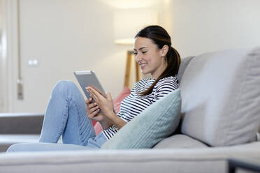 Smiling woman using digital tablet on sofa in living room - EIF01145