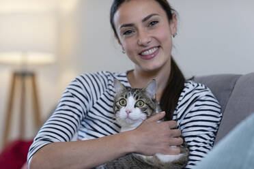 Smiling woman with tabby cat on sofa at home - EIF01147