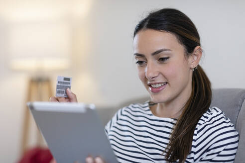 Frau hält Kreditkarte beim Einkaufen auf digitalem Tablet im Wohnzimmer - EIF01150