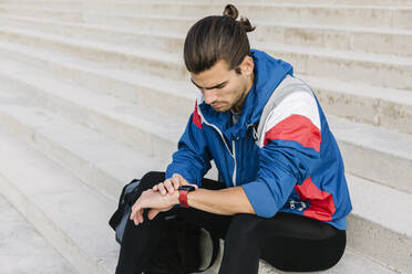 Sportler überprüft seine Smartwatch, während er auf einer Treppe sitzt - XLGF01969