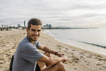 Sportsman smiling while sitting on beach - XLGF01973