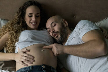 Mann berührt den Unterleib einer schwangeren Frau, während sie zu Hause im Bett liegt - WPEF04610