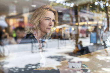 Nachdenkliche Frau schaut durch das Fenster, während sie in einem Café sitzt - WPEF04617