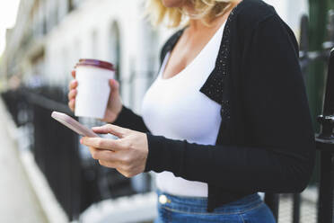 Frau mit Einweg-Kaffeebecher und Smartphone - WPEF04619