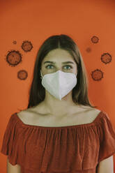 Teenage girl wearing protective face mask amidst virus on red background - LIFIF00045