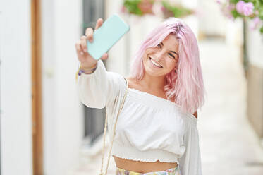 Smiling woman with pink hair taking selfie through smart phone - KIJF03933