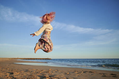 Carefree woman jumping at beach during sunset - KIJF03946