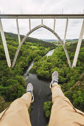 Spanien, Provinz A Coruna, Vedra, Persönliche Perspektive eines Mannes, der über einem Tal sitzt, das den Fluss Ulla überspannt, mit der Gundian-Brücke im Hintergrund - RSGF00710