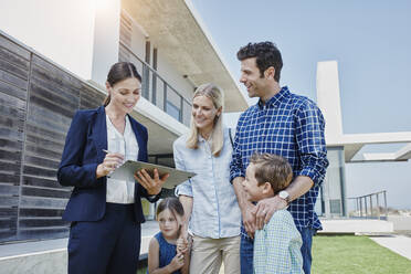 Female restate agent showing notepad to family in front of villa - RORF02717