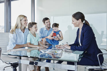 Smiling female real estate agent discussing with family sitting at table - RORF02742