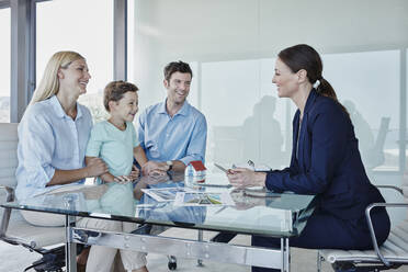 Happy family discussing with female real state agent while sitting at table - RORF02744