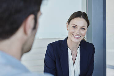 Lächelnde Geschäftsfrau, die einen Mann ansieht, während sie mit ihm diskutiert - RORF02747