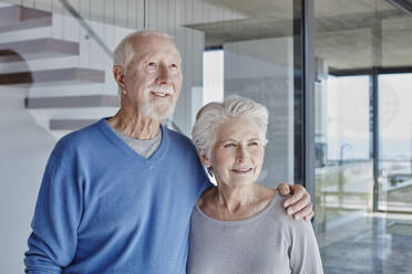 Smiling senior couple standing together in front of glass wall - RORF02773