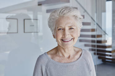 Happy senior woman standing in front of glass wall - RORF02774