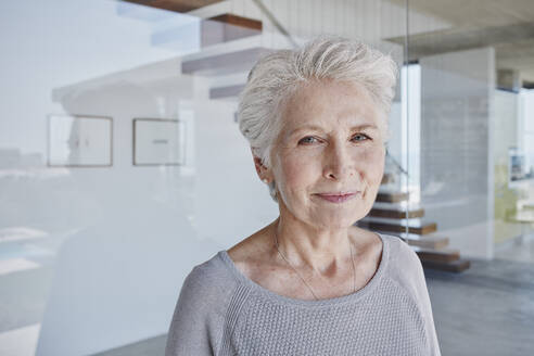 Senior woman with white hair standing in front of glass wall - RORF02775