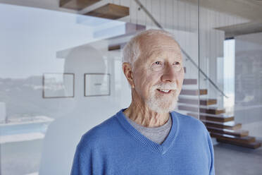 Smiling senior man standing in front of glass wall looking away - RORF02777