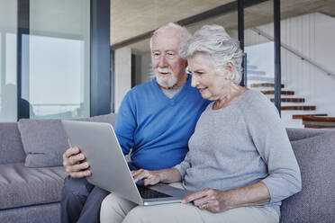 Senior couple using laptop sitting on sofa in living room - RORF02793