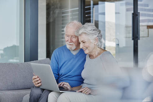 Smiling senior couple using laptop sitting in living room at home - RORF02795