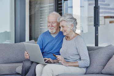 Smiling senior couple doing online shopping while sitting in living room at home - RORF02797