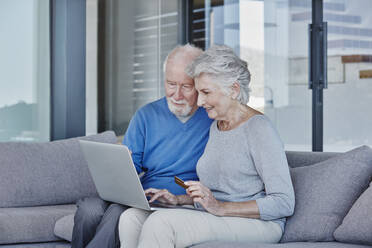 Älterer Mann und Frau benutzen Laptop beim Online-Shopping zu Hause - RORF02798