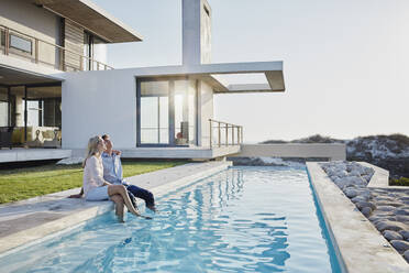 Relaxed couple sitting together at pool in backyard - RORF02815