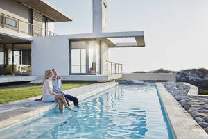 Relaxed couple sitting together at pool in backyard - RORF02815