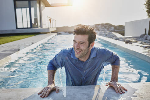 Cheerful man coming out of swimming pool while looking away - RORF02818