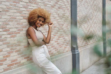 Smiling woman with hand in hair leaning on wall - AGOF00115