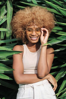 Smiling young woman wearing sunglasses standing amidst leaves - AGOF00121