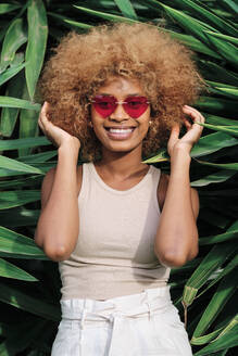 Smiling woman with hand in hair standing amidst leaves - AGOF00122