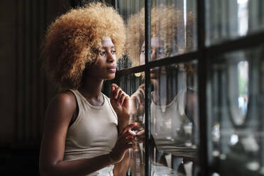 Nachdenkliche Afro-Frau, die durch das Fenster ihres Hauses schaut - AGOF00124