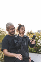 Mädchen macht Selfie mit Vater durch Smartphone im Park - JAQF00662