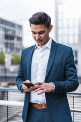 Businessman working on smart phone in front of railing - DIGF15670