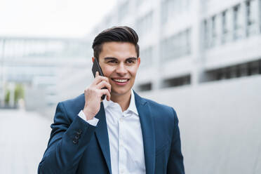 Lächelnder Geschäftsmann, der im Freien stehend mit seinem Mobiltelefon spricht - DIGF15679