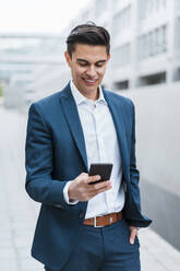 Männlicher Unternehmer, der ein Smartphone benutzt, während er im Freien steht - DIGF15681