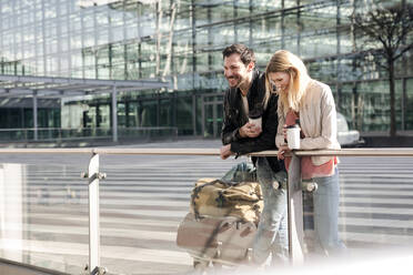 Smiling young couple having coffee while standing outside airport - AUF00711