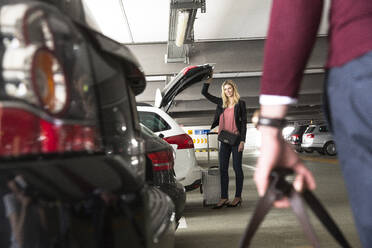 Smiling woman opening car trunk while waiting for boyfriend at airport parking lot - AUF00712