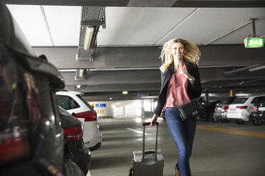 Junge Frau läuft mit Rollkoffer auf einem Flughafenparkplatz - AUF00713