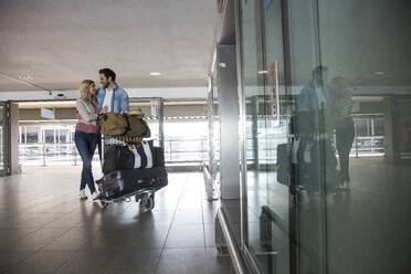 Glückliches junges Paar mit Gepäckwagen im Flughafenterminal - AUF00721