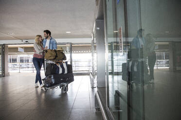 Happy young couple with luggage trolley at airport terminal - AUF00721