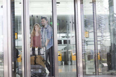 Young couple with luggage trolley at airport terminal - AUF00726