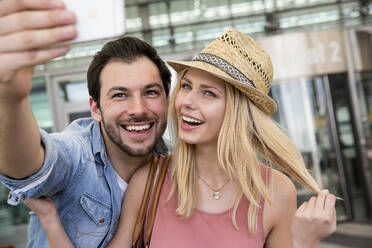Junges Paar nimmt Selfie durch Smartphone außerhalb des Flughafenterminals - AUF00730