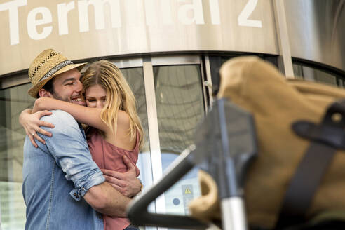 Junges Paar, das sich vor dem Flughafenterminal umarmt - AUF00735