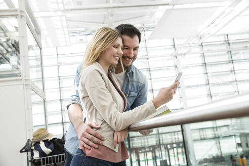 Young couple looking at smart phone in airport departure area - AUF00738