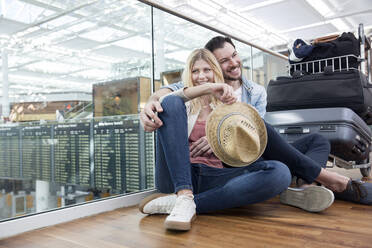 Young couple sitting on floor waiting in airport depature area - AUF00740