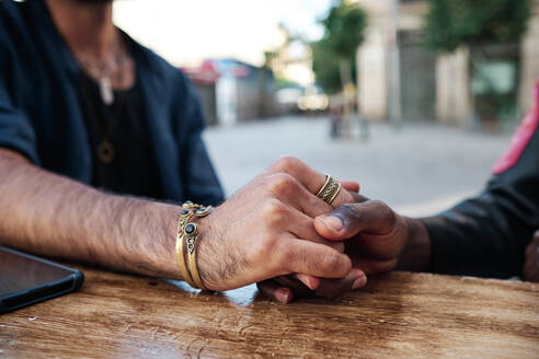 Gay couple holding hands on table at sidewalk cafe - AGOF00125